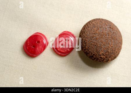Two red buttons and a rough stone rest on soft beige fabric, creating a serene scene. Stock Photo