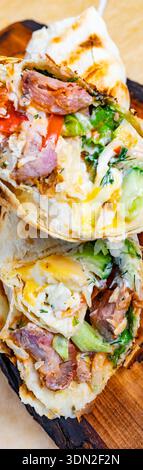 Tacos filled with various meats and fresh vegetables are placed on a wooden board ready to eat. Stock Photo