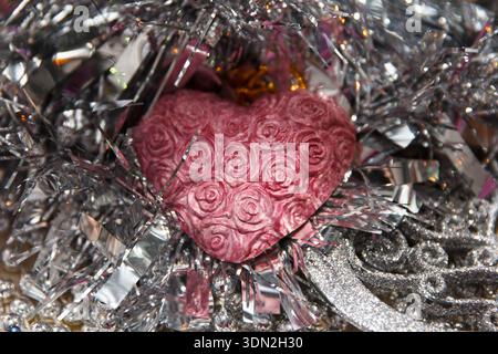 A pink beautiful heart with rose patterns surrounded by shiny silver tinsel. Scene conveys a festive atmosphere, suitable for celebrations or romantic Stock Photo