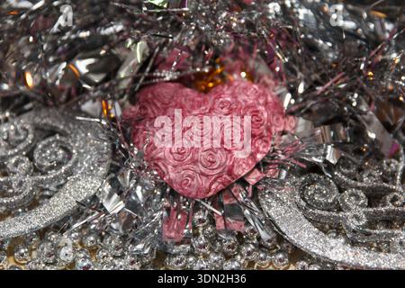 A pink heart with rose patterns surrounded by shiny silver tinsel. Scene conveys a festive atmosphere, suitable for celebrations or romantic occasions Stock Photo