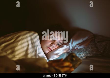 young woman uses smartphone at night while lying in bed Stock Photo