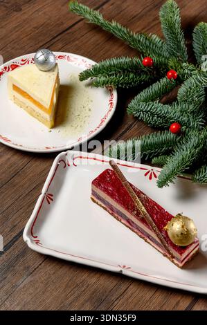 Two different mousse cakes on white plates with New Year's decor. Berry and citrus desserts with chocolate and pastry balls next to a spruce branch Stock Photo