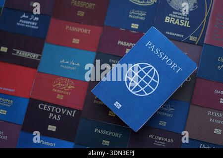 Fictional passport book travel document on big amount of real passport covers of various different countries. Expired passports in big pile close up. Stock Photo