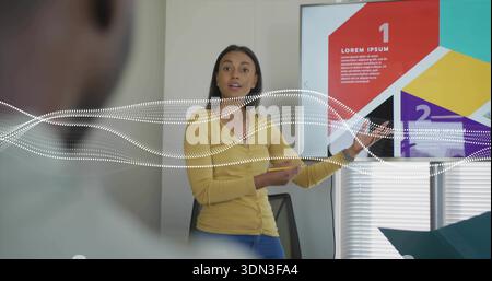 Talking woman in yellow cardigan, jeans pointing at display at office, numbered slide, teal folder Stock Photo