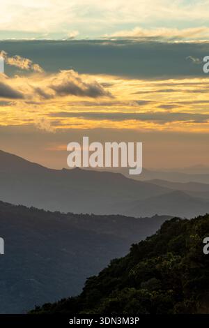 Sunset over layered mountain ranges with dramatic clouds and golden light breaking through mist. Atmospheric landscape, Boquete, Chiriqui, Panama. Stock Photo