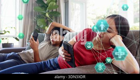 Reclining Asian couple using smartphones on sofa at home, in red shirt, gray tee, medical hexes Stock Photo