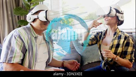 Exploring couple using blue globe on couch in living room, VR headsets, striped and plaid shirts Stock Photo