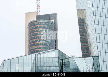Modern glass office buildings with reflective windows and geometric architecture against a cloudy sky in Vilnius, symbolizing corporate growth, urban Stock Photo
