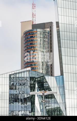 Modern glass office buildings with reflective windows and geometric architecture against a cloudy sky in Vilnius, symbolizing corporate growth, urban Stock Photo