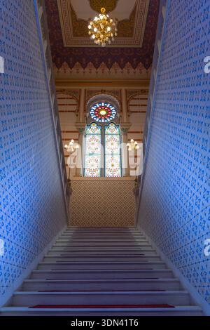 View of a staircase with intricate blue patterns on the walls leading to a stained glass window and ornate ceiling, Sarajevo, Federacija Bosne i Herce Stock Photo