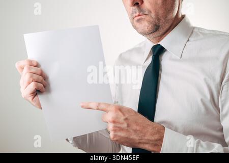 Serious businessman pointing at blank white paper sheet mockup, selective focus Stock Photo