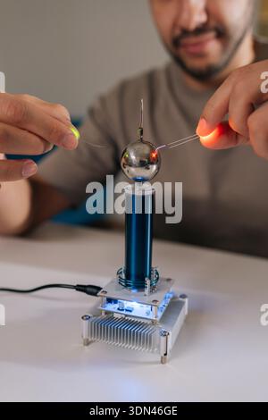Vertical shot of scientist holding two leds near mini tesla coil, observing electrostatic discharge and electrical sparks illuminating light-emitting Stock Photo