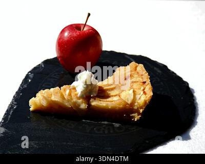 Slice of apple tart on a dark slate board with a whole red apple behind it. Stock Photo