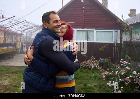 Middle-aged man hugging elderly mother in front of rural village house Stock Photo
