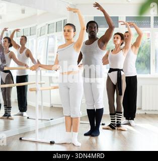 Group mastering third position at barre in ballet studio Stock Photo