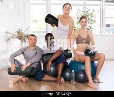 Happy portrait of group of four people wearing activewear with mats and soft balls going to do yoga in gym Stock Photo