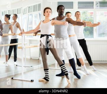 Woman practicing battement tendu at barre during ballet group class Stock Photo