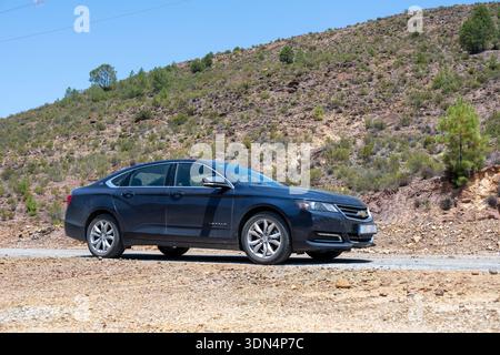 Riotinto, Spain - 3 July 23: A black Chevy Impala sedan parked on a gravel road with a hilly landscape in the background Stock Photo