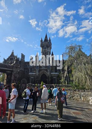 EDITORIAL USE ONLY-ORLANDO, FLORIDA-JANUARY 2026: A wide-angle view of the towering Frankenstein Manor, the centerpiece of the Dark Universe land at Universal Epic Universe. The image showcases the intricate, weathered, Gothic architecture of the manor, featuring a central clock tower, jagged spires, and a grand arched entrance. Visitors in casual attire are seen in the foreground on the cobblestone plaza of Darkmoor Village, contrasted against a vibrant blue sky with wispy clouds. The scene captures the immersive, moody atmosphere of the Universal Monsters-themed area during a bright day. Stock Photo
