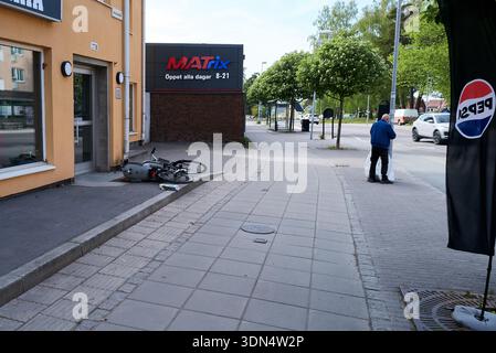A man is standing on the sidewalk in front of a Matrix store. A bicycle has fallen on the sidewalk. Nynashamn, Stockholm County, Sweden, 25 May 2025 Stock Photo