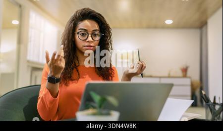Woman Engaged in a Virtual Meeting in a Modern Office Space With a Laptop and a Notepad Stock Photo