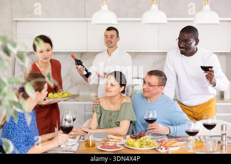 Cheerful friends enjoying wine and conversations in home kitchen Stock Photo