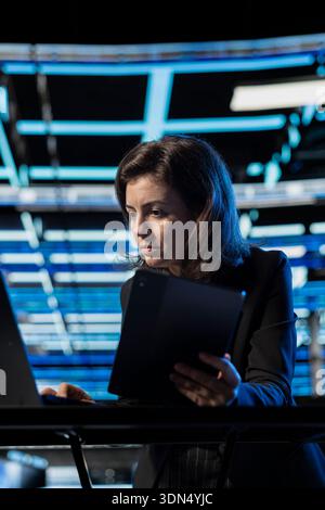 Configuring firewall, devices and programmer in data center verifying security patches. Applying equipment vulnerability scans, IT expert, laptop and tablet in server hub Stock Photo