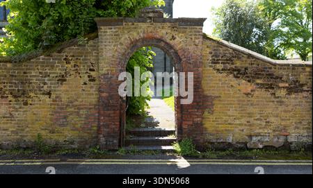 Old Brick Arch Gate Through Wall Leading to Garden Path and Sunlit Courtyard Stock Photo