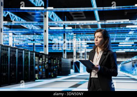 Data center manager using tablet, managing server virtualization. System administrator using device in server room, doing upgrades sustaining long term infrastructure reliability Stock Photo