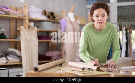 Woman tailor draw dress pattern on paper and participate in creating ...