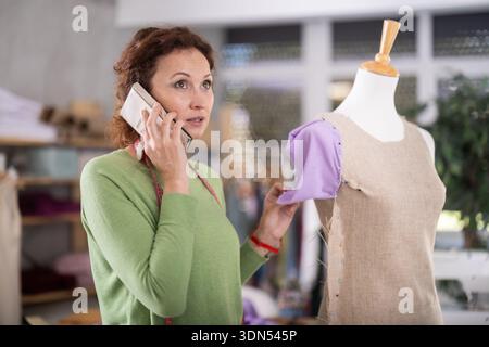Female tailor talking on phone in sewing workshop Stock Photo