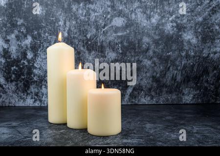 Three lit pillar candles arranged in depth on dark textured background. Minimal wellness concept with copy space. Stock Photo