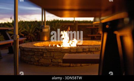 Cozy evening atmosphere with a burning gas fire pit on a stone patio in a luxury garden in Rancho Palos Verdes, California. Stock Photo