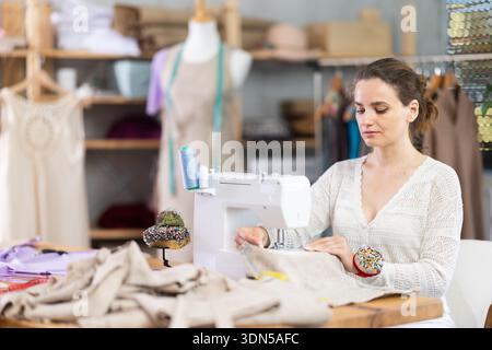 Female tailor using sewing machine to make garment in studio Stock Photo
