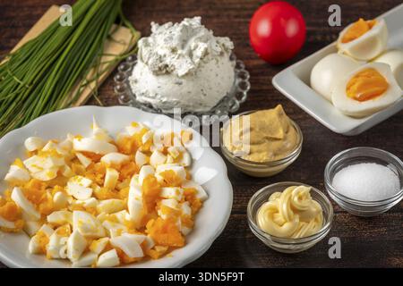 Sliced Easter eggs and fresh ingredients for a spread arranged on a wooden table Stock Photo