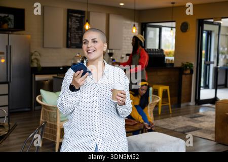 Diverse group at cafe with woman holding cup and smartphone, barista operating espresso machine Stock Photo