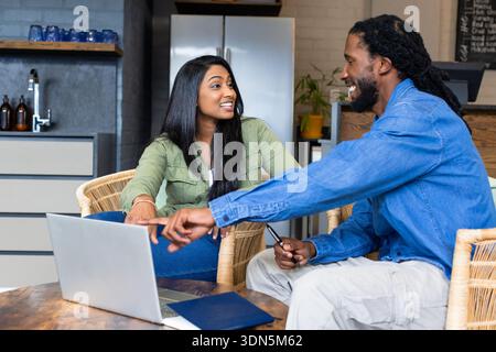 Diverse coworkers collaborating on project at modern kitchen lounge using laptop, notebook and pen Stock Photo