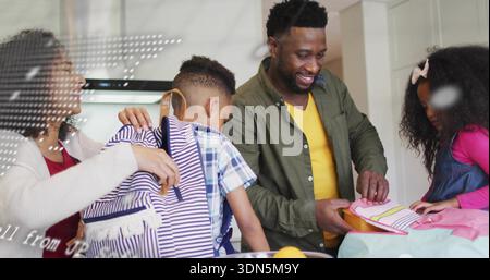 Helping woman in cardigan adjusting striped backpack on boy in kitchen, placing pink lunchbox Stock Photo