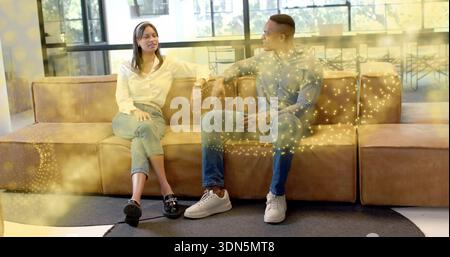 Chatting two adults sitting on brown leather sofa in lounge, wearing grey hoodie, white blouse Stock Photo