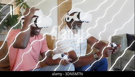 Playing father-son wearing VR headsets, pink t-shirt and striped polo on sofa, holding controllers Stock Photo