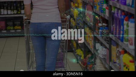 Pushing metal cart, shopper wearing white top, blue jeans walking grocery aisle, purple bag Stock Photo