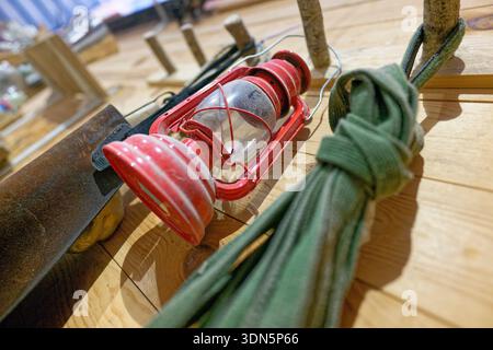 A wooden shelf and hooks on a timber wall hold a red metal lantern and a leather apron, all coated with fine sawdust that signals active woodworking n Stock Photo