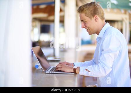 Managing online booking, business man smiling while using a laptop at a cafe counter or bar in holiday location, with a casual ambiance, nightlife rev Stock Photo