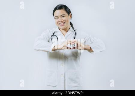Smiling asian female doctor making heart shape isolated. Asian healthcare worker gesturing heart Stock Photo