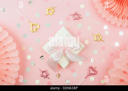 Gift box, candles, colorful confetti and tissue paper fans on coral pink background. Birthday party concept. Top view, flat lay. Stock Photo