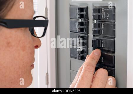 Closeup view of a woman operating a residential electrical panel inside a home. Concept of household electricity, power control, safety, maintenance, Stock Photo