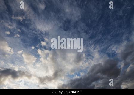 A wide-angle view of various cloud formations, including wispy cirrus and dark cumulus, against a brilliant dark blue sky. Stock Photo