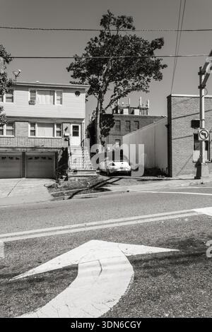 Dramatic black and white street scene in Fort Lee, NJ, featuring a white convertible parked between a multi-family home and a brick commercial buildin Stock Photo