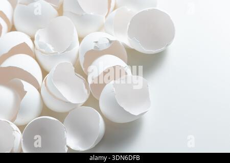 Small pieces of white eggshells lay on a clean white surface. These shells are left from eggs used in cooking. Stock Photo
