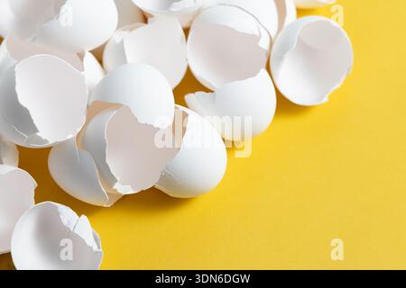 Broken eggshells are spread across a yellow surface. The shells are white and show cracks, suggesting recent use in a cooking or baking activity. Stock Photo